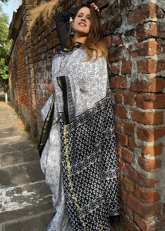 Woman in a black and white patterned dress leaning against a brick wall.