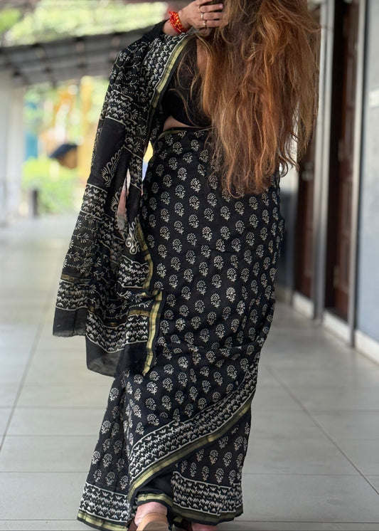 Woman in a black and white patterned saree standing outdoors.