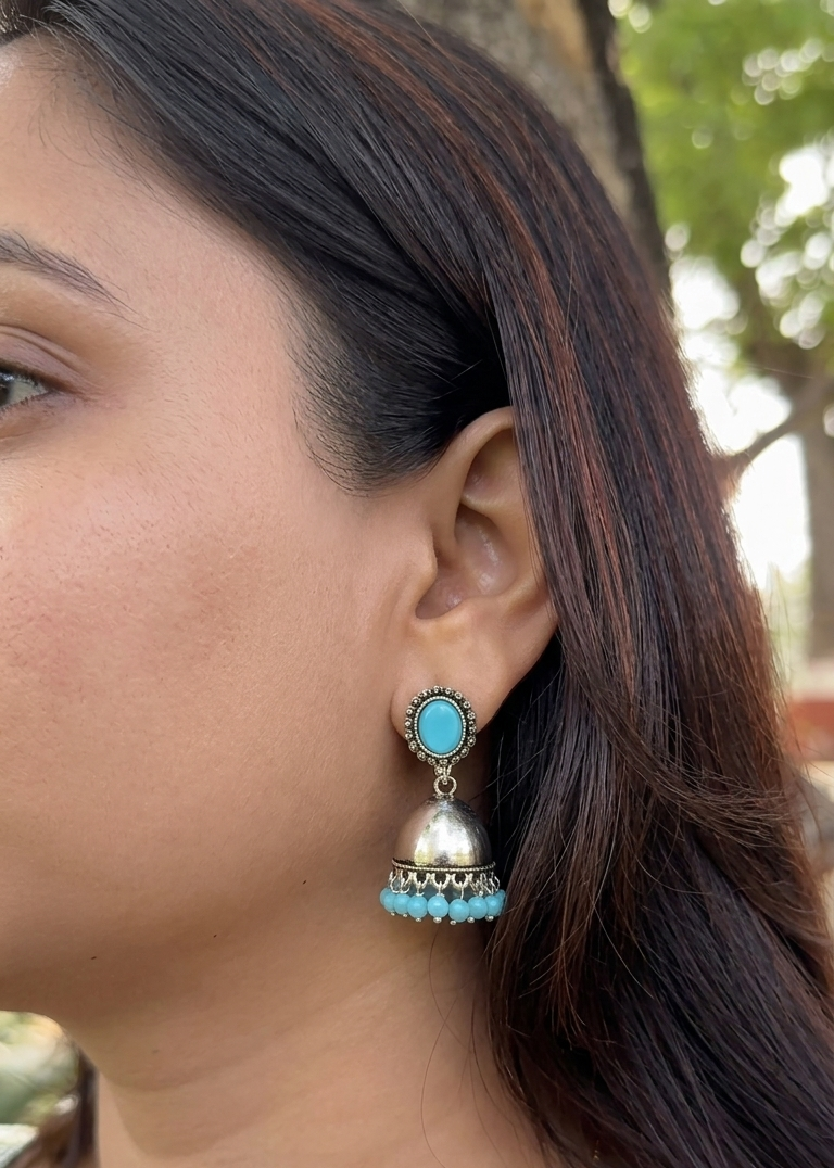 Close-up of a woman wearing turquoise and silver earrings with a blurred natural background