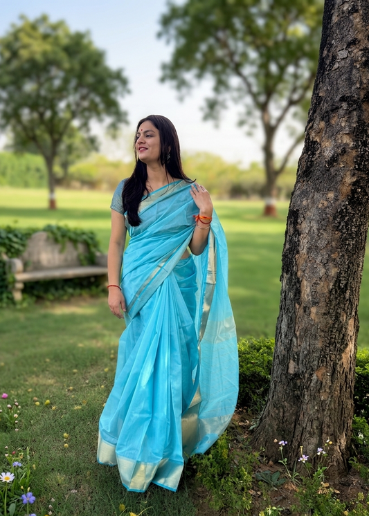 Woman in a blue saree standing outdoors near a tree