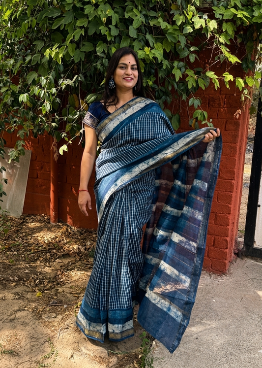Woman in a blue saree standing outdoors with greenery in the background