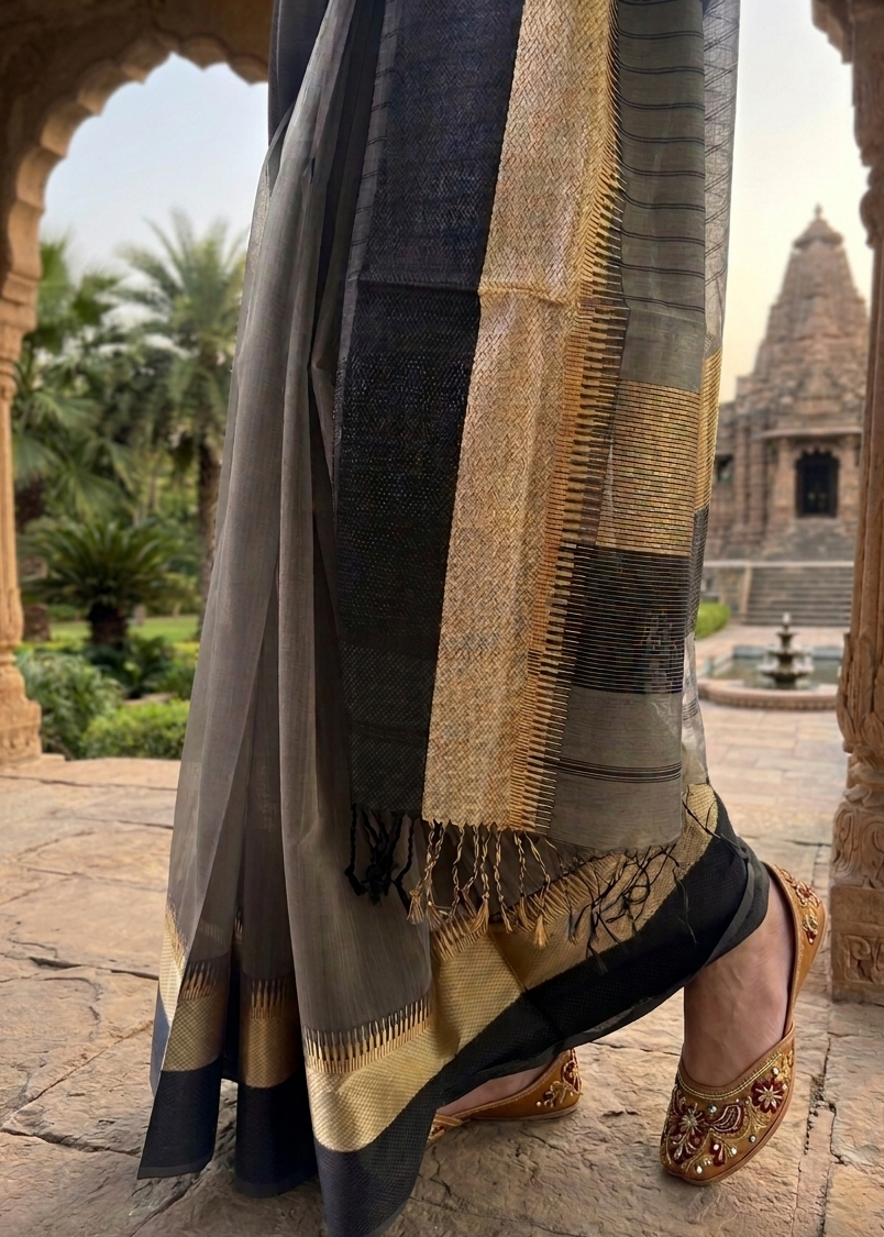Person wearing a traditional saree with gold and black patterns in an outdoor setting.