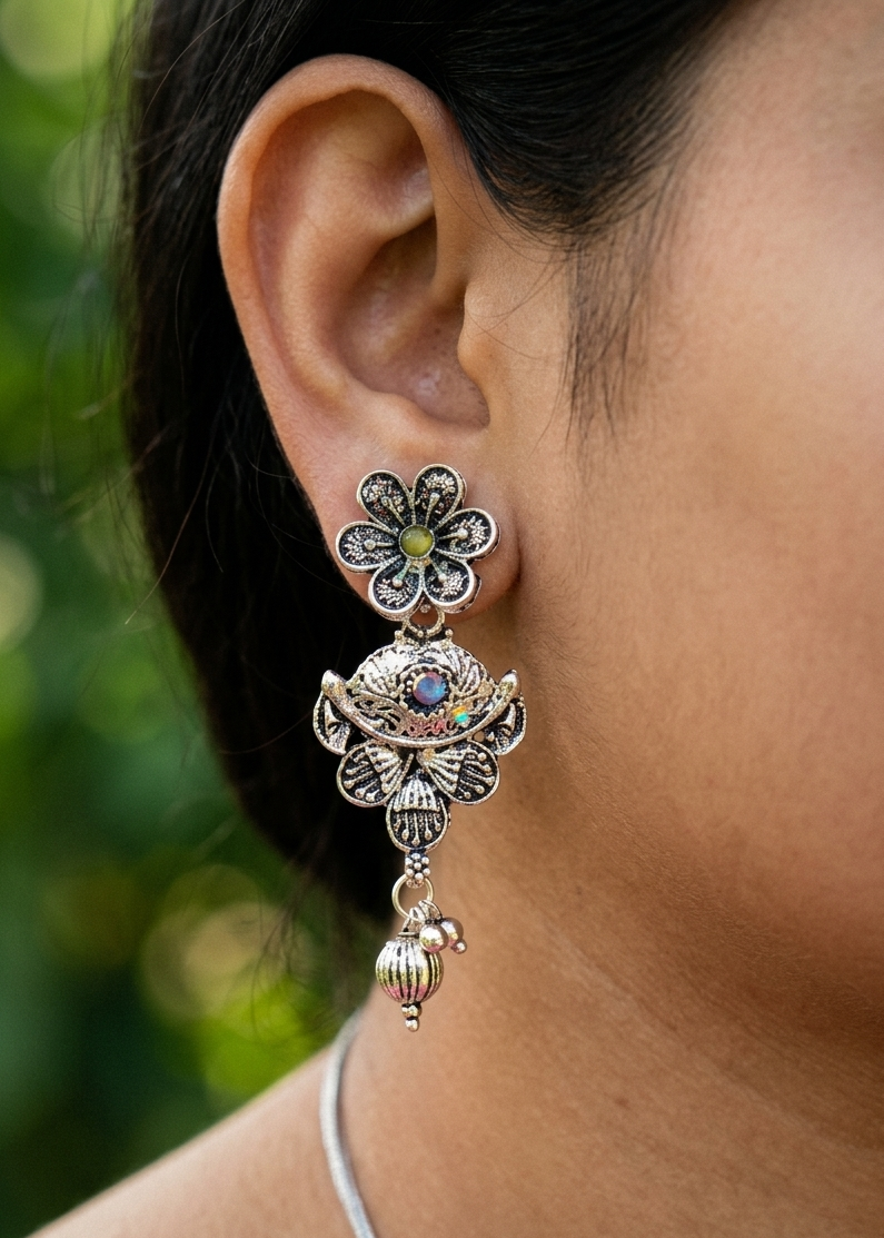 Close-up of a person wearing an ornate silver earring with a green gemstone against a blurred natural background.