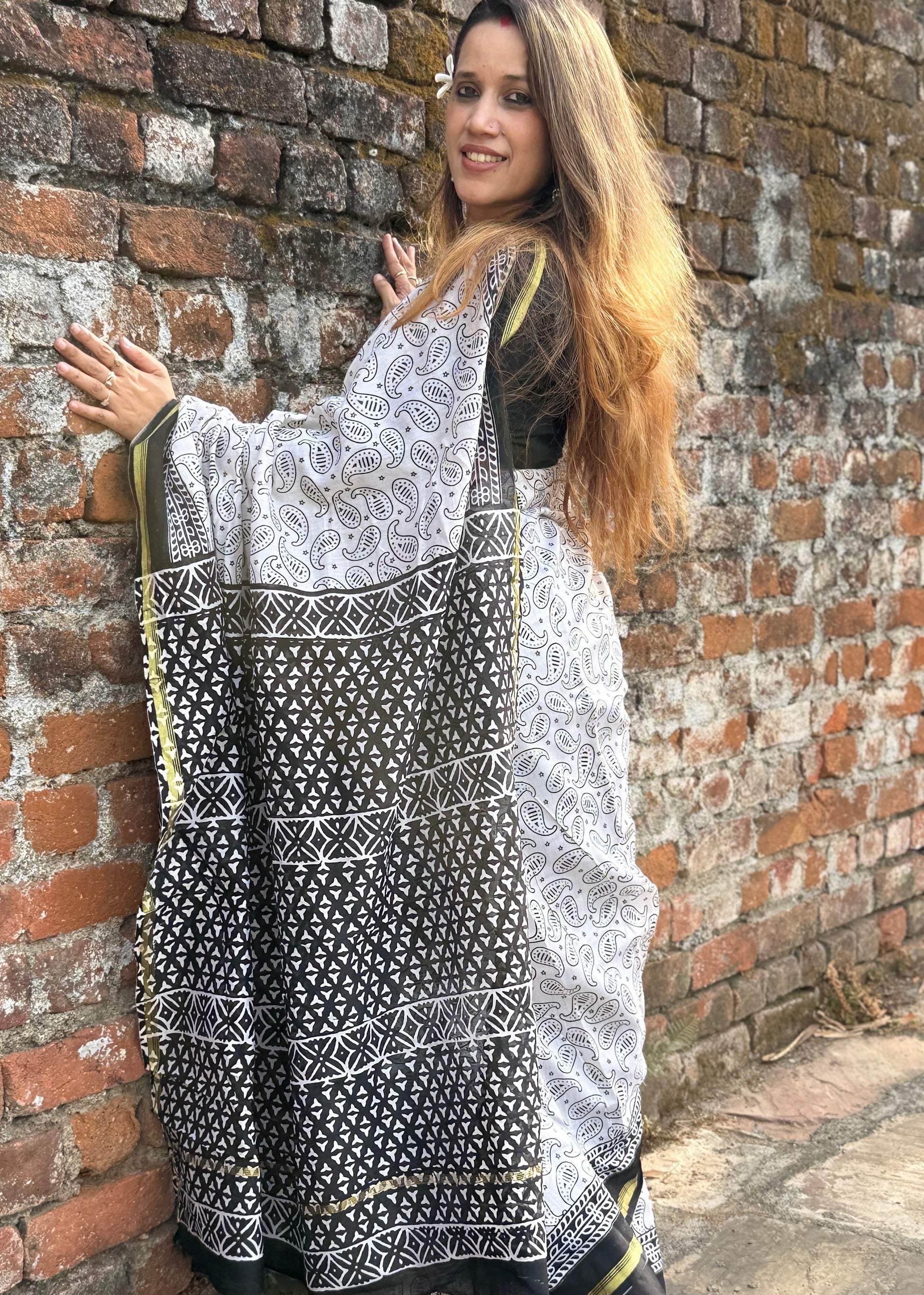 Woman holding a black and white patterned scarf against a brick wall.