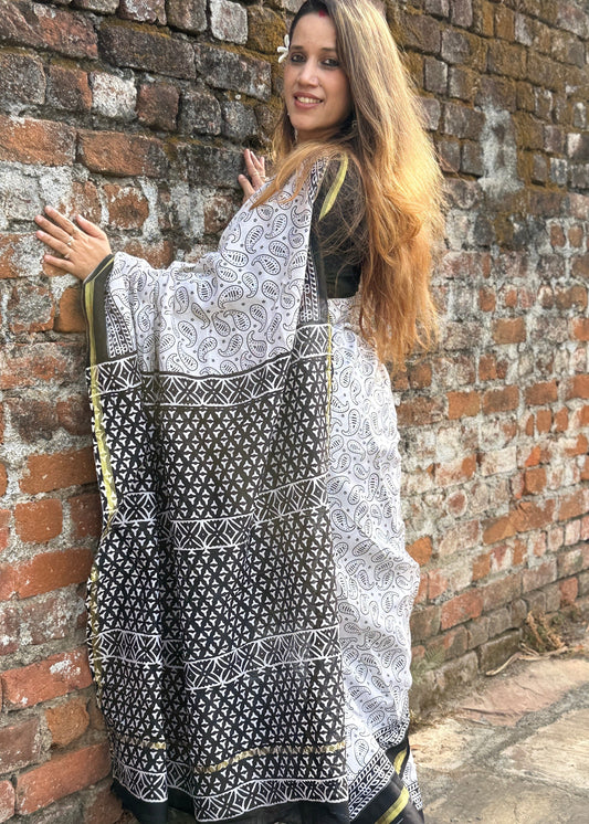 Woman holding a black and white patterned scarf against a brick wall.