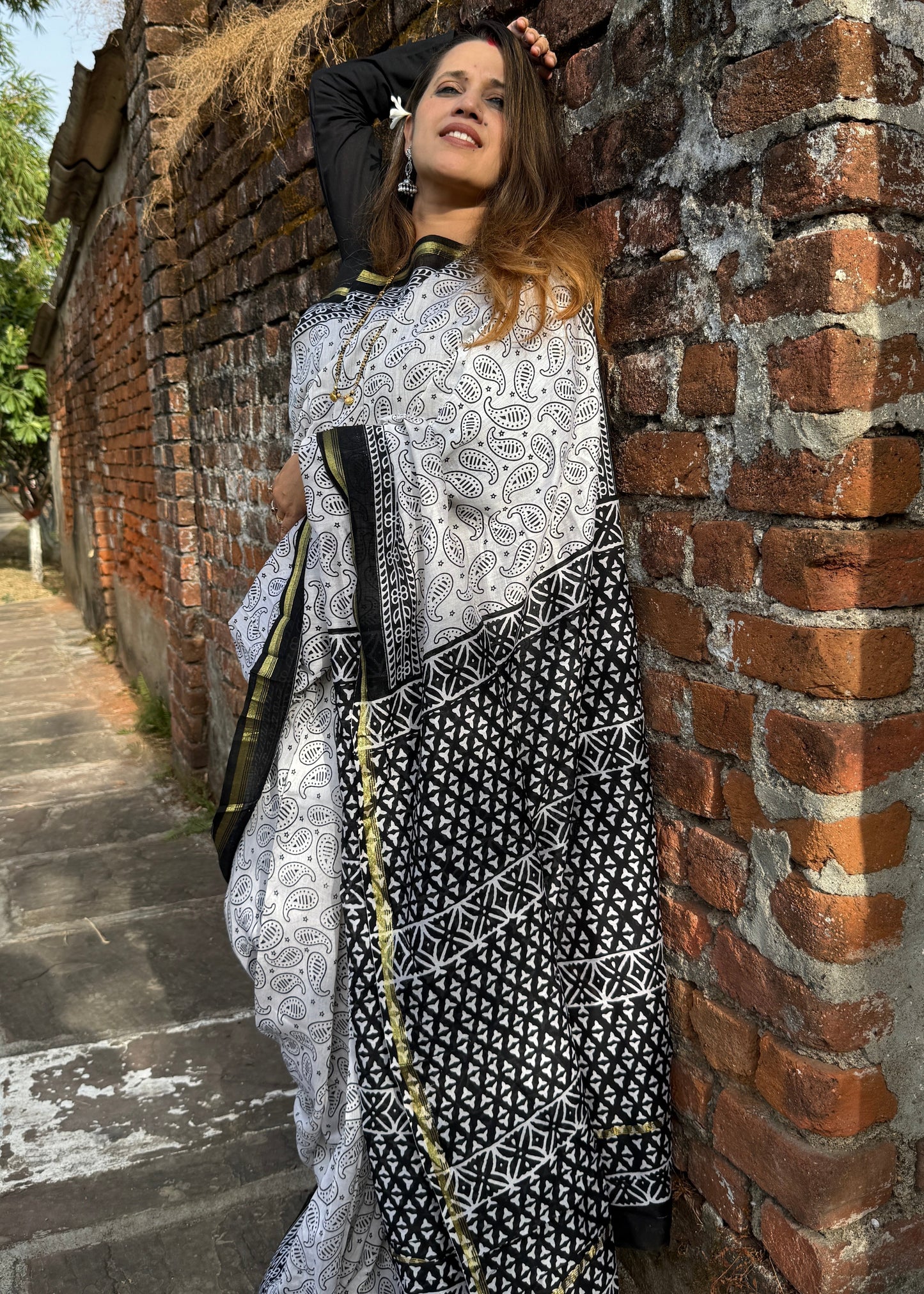 Woman in a black and white patterned dress leaning against a brick wall.