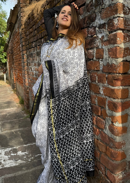 Woman in a black and white patterned dress leaning against a brick wall.