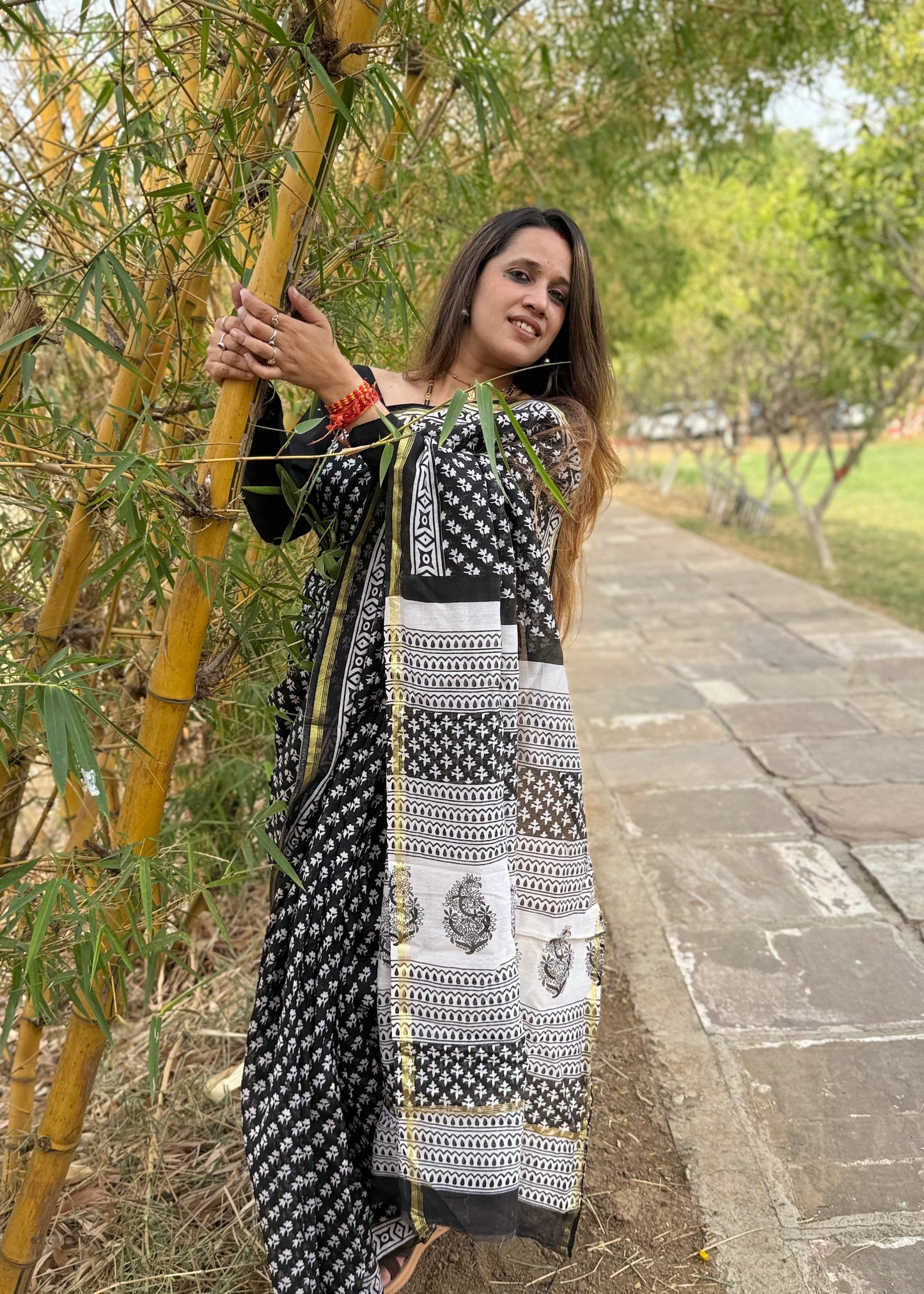 Woman in a black and white patterned dress standing next to a bamboo plant on a path.