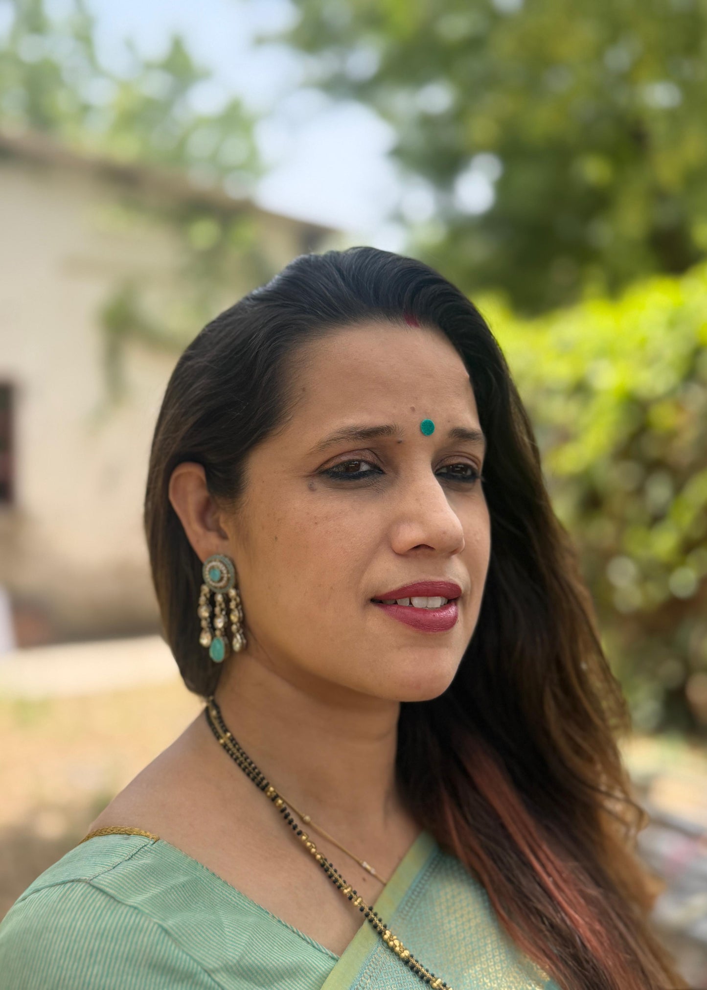 Woman wearing a green saree with a blurred outdoor background