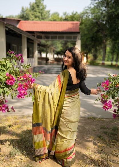 Woman in a saree standing outdoors with flowers and a building in the background