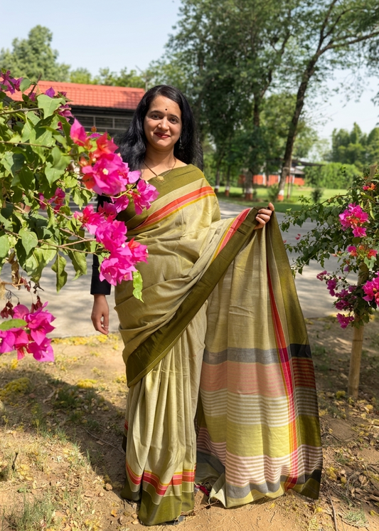 Woman in a traditional saree holding pink flowers outdoors with greenery around