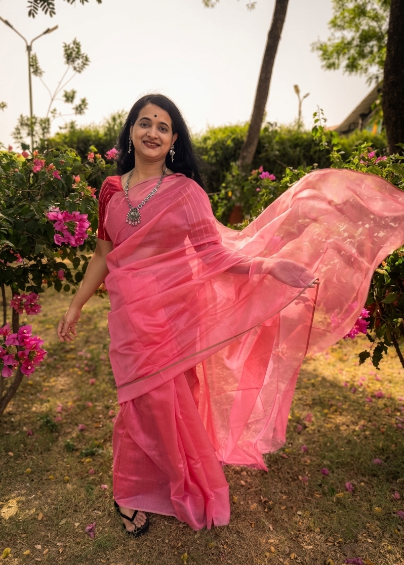 Woman in a pink saree standing outdoors with flowers and greenery around