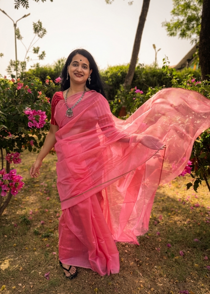 Woman in a pink saree standing outdoors with flowers and greenery around