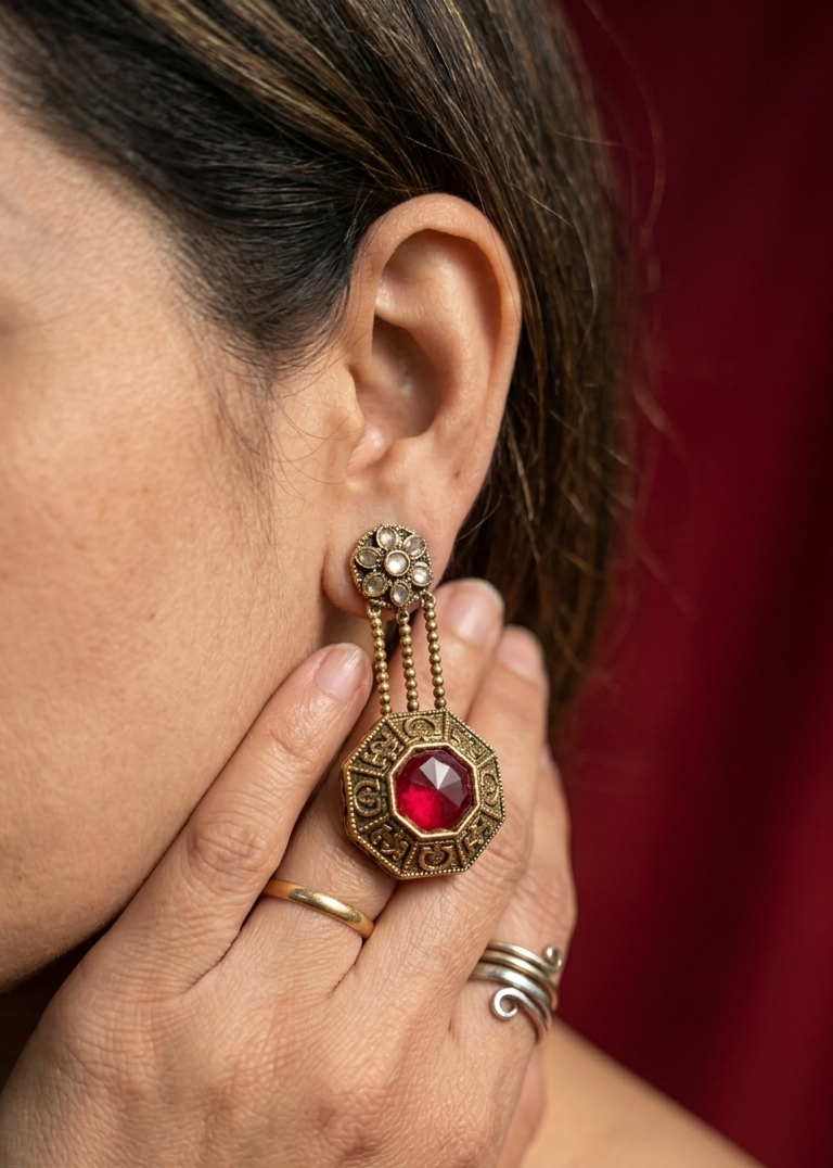 Close-up of a person wearing an ornate earring with a red gemstone against a blurred background.