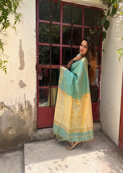 Woman in a green and yellow saree standing in front of a red door with floral decorations.