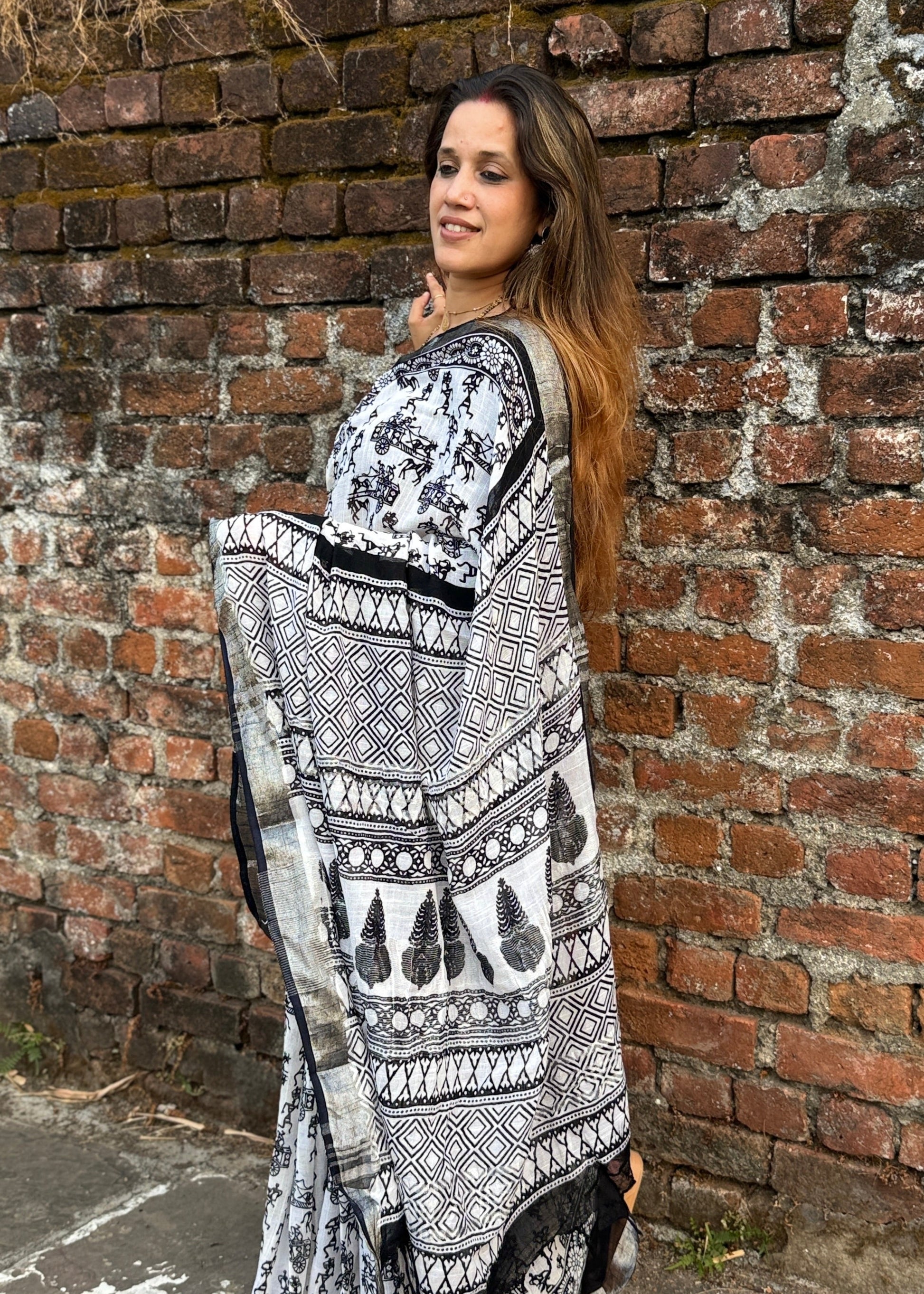 Woman wearing a black and white patterned dress leaning against a brick wall.