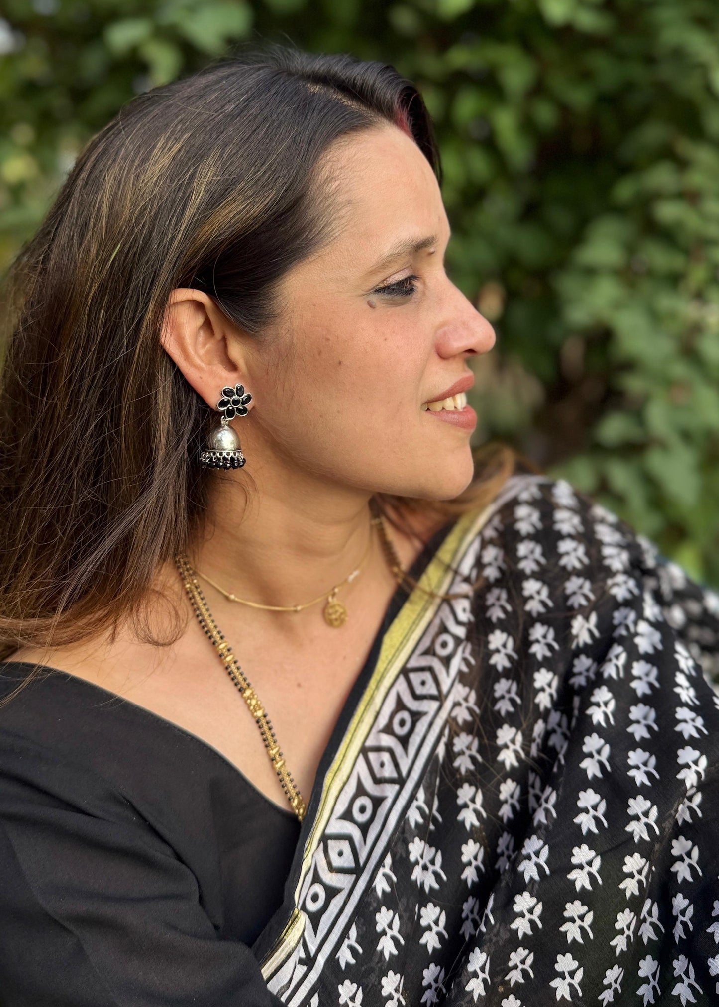 Woman wearing a black and white patterned saree with greenery in the background