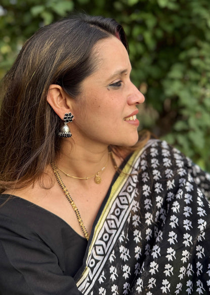 Woman wearing a black and white patterned saree with greenery in the background