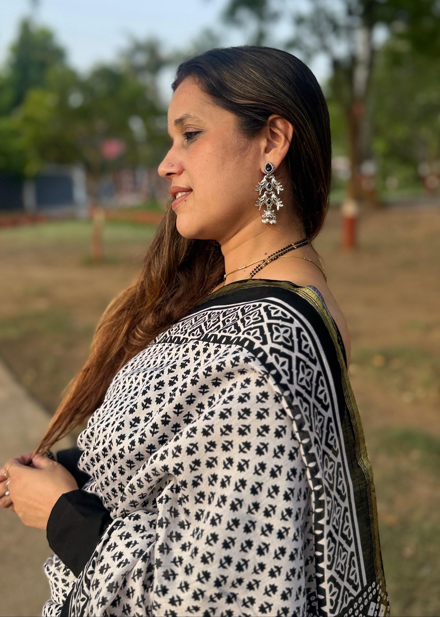Woman wearing a black and white patterned shawl outdoors with trees in the background