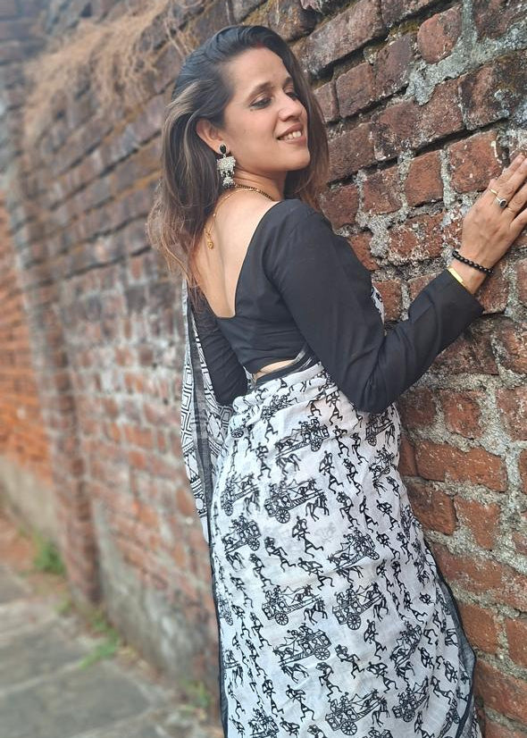 Woman in a black top and floral skirt leaning against a brick wall.